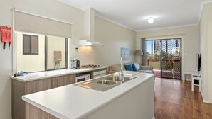 A modern kitchen with a central island, a dining area with a sofa, and a view of a balcony. - Discovery Parks - Adelaide Beachfront (Semaphore Park)