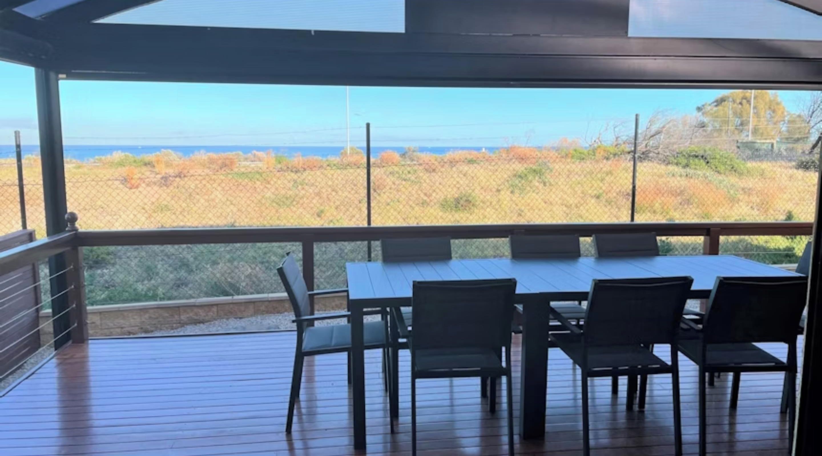An outdoor deck with a table and chairs, overlooking a coastal landscape.