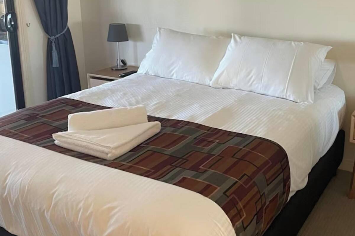 A neatly made bed with white linens, a brown patterned bedspread, and two bedside lamps on wooden nightstands.