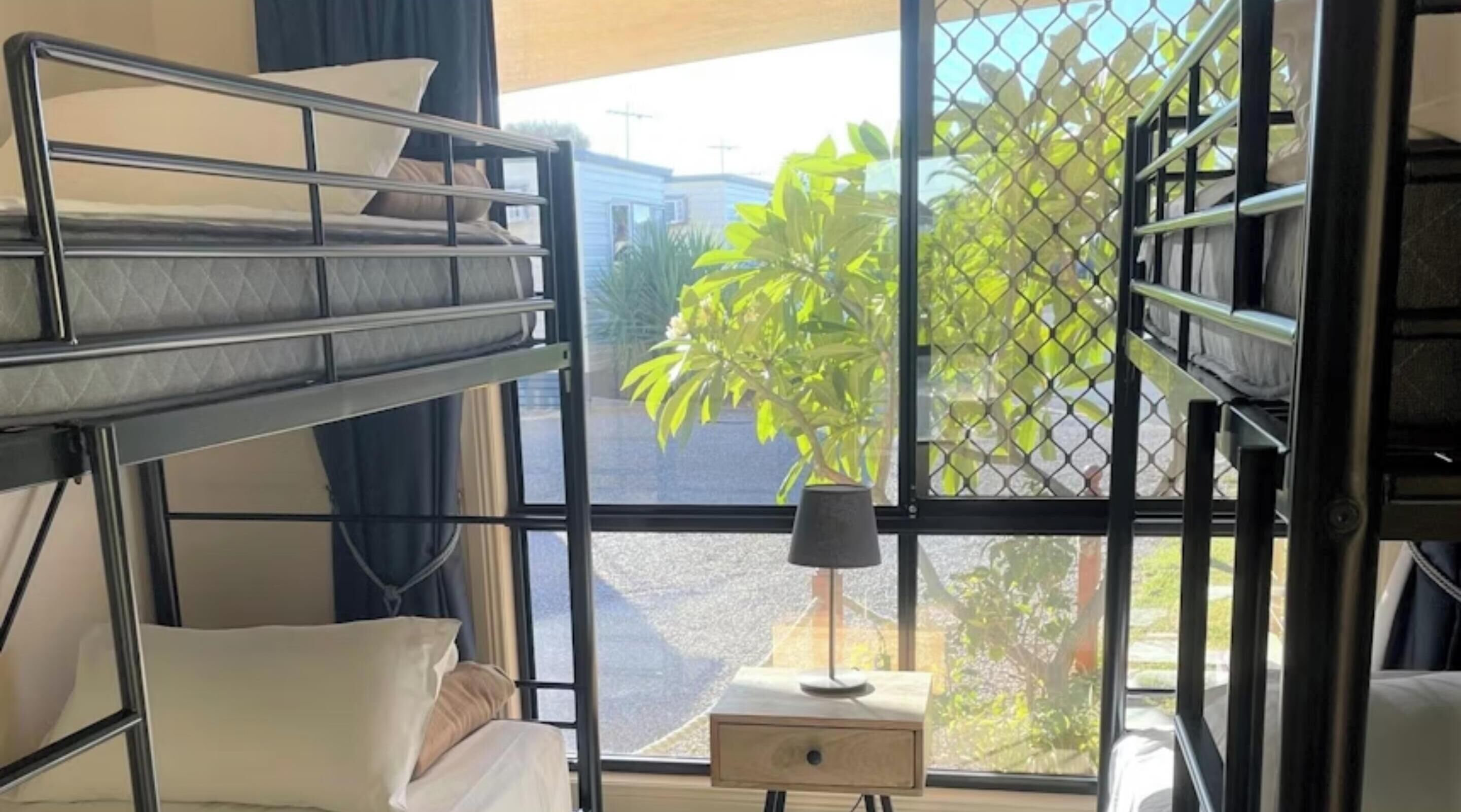 A bunk bed room with a window view of a garden and a small table with a lamp.