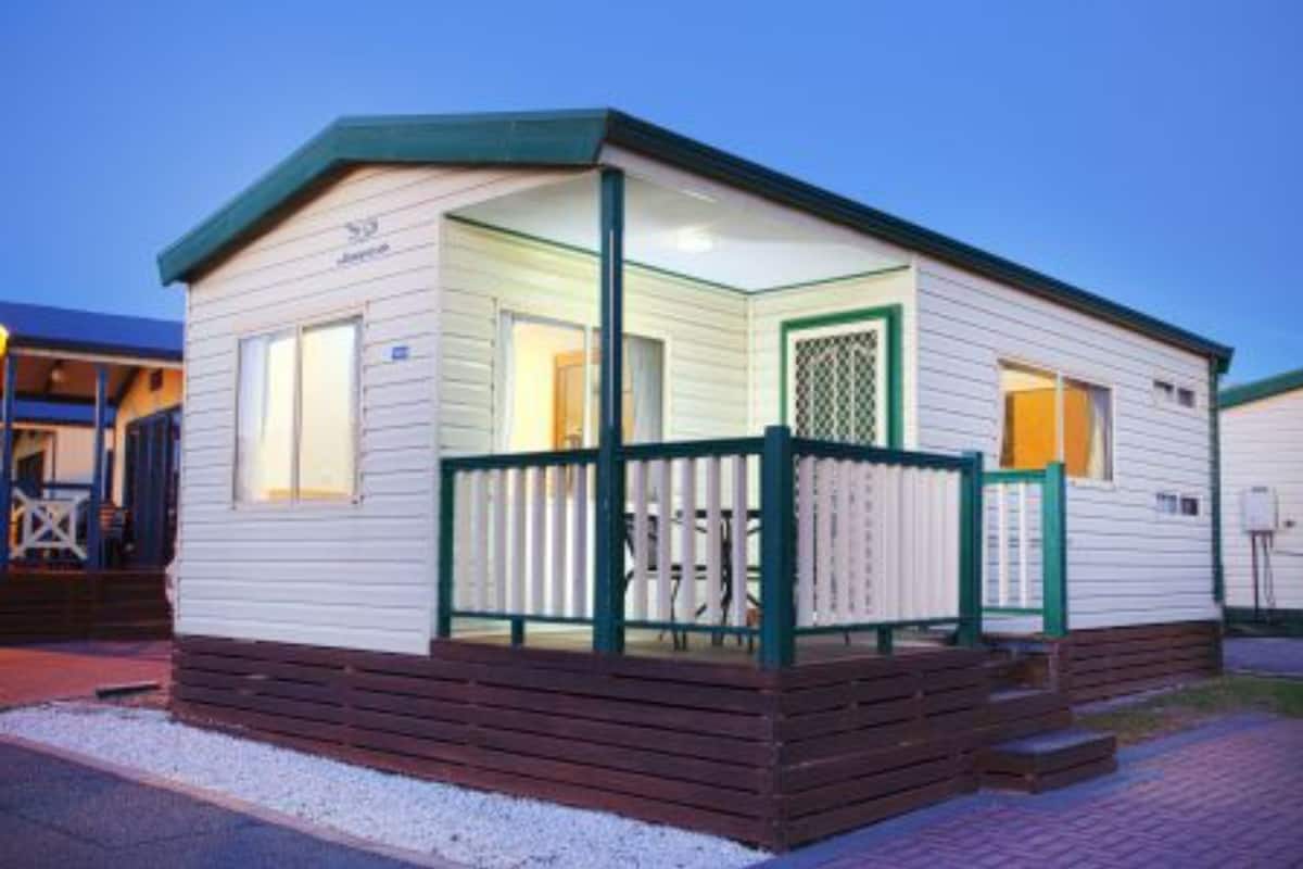 A small, single-story mobile home with a porch and a fenced deck area.