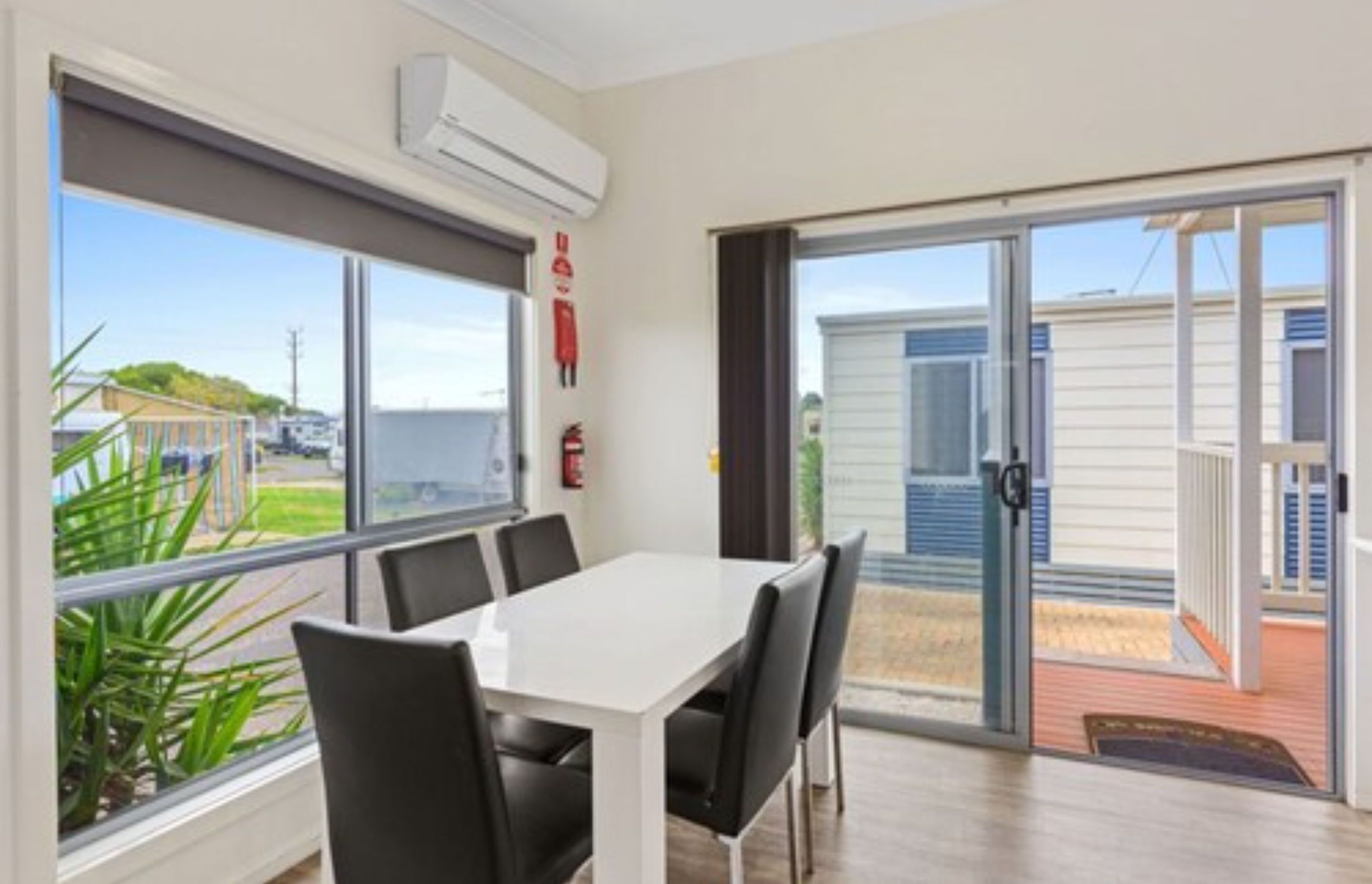 A room with a white table and chairs, a sliding glass door to the outside, and a fire extinguisher on the wall.
