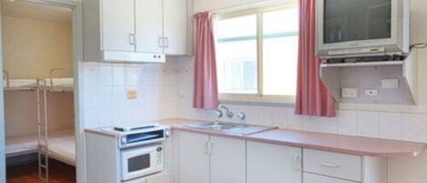 A compact kitchen with white cabinets, a microwave, a stove, a sink, and a television mounted above the counter.