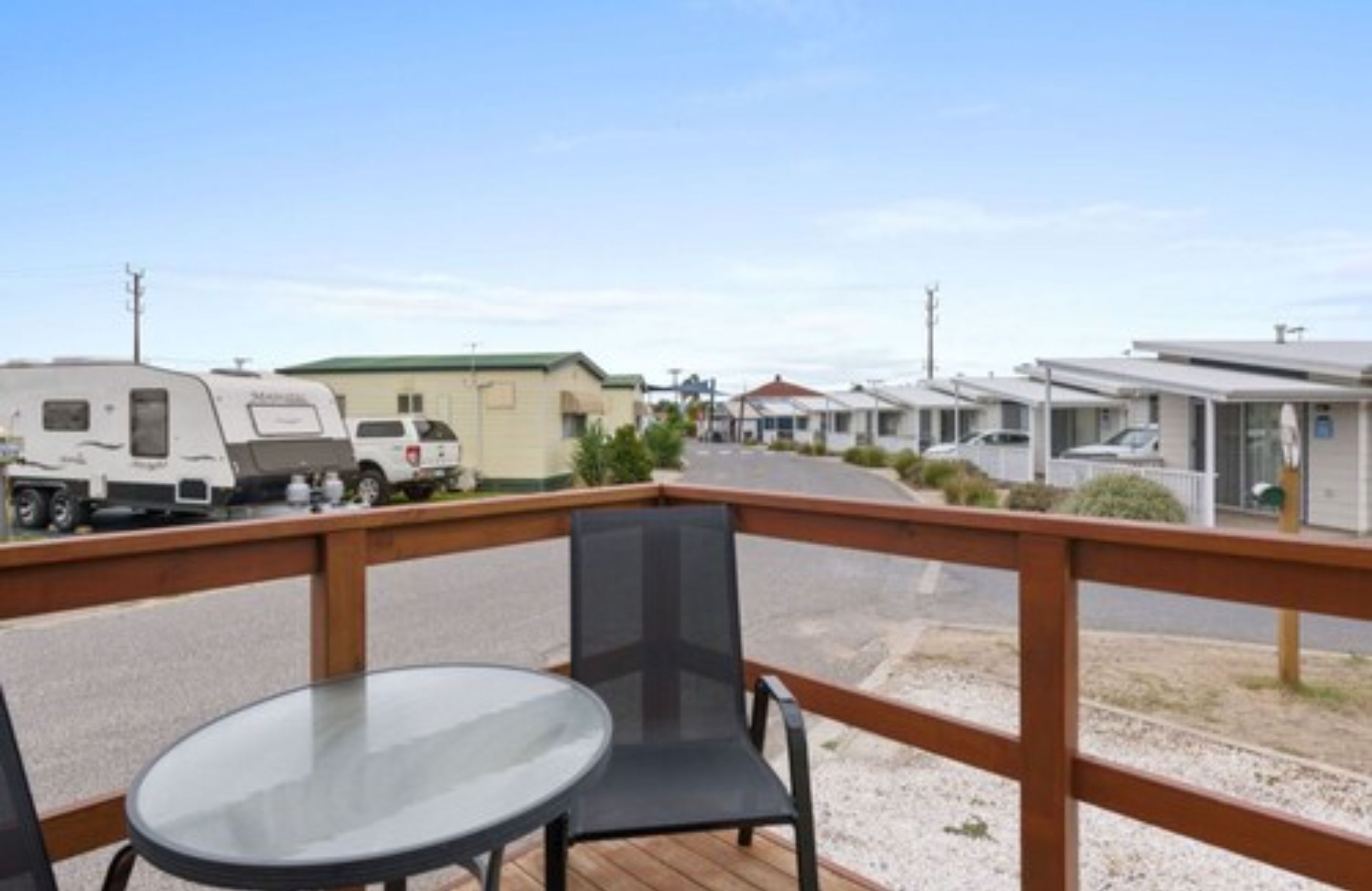 A deck with a table and chairs overlooking a parking area with RVs and mobile homes.