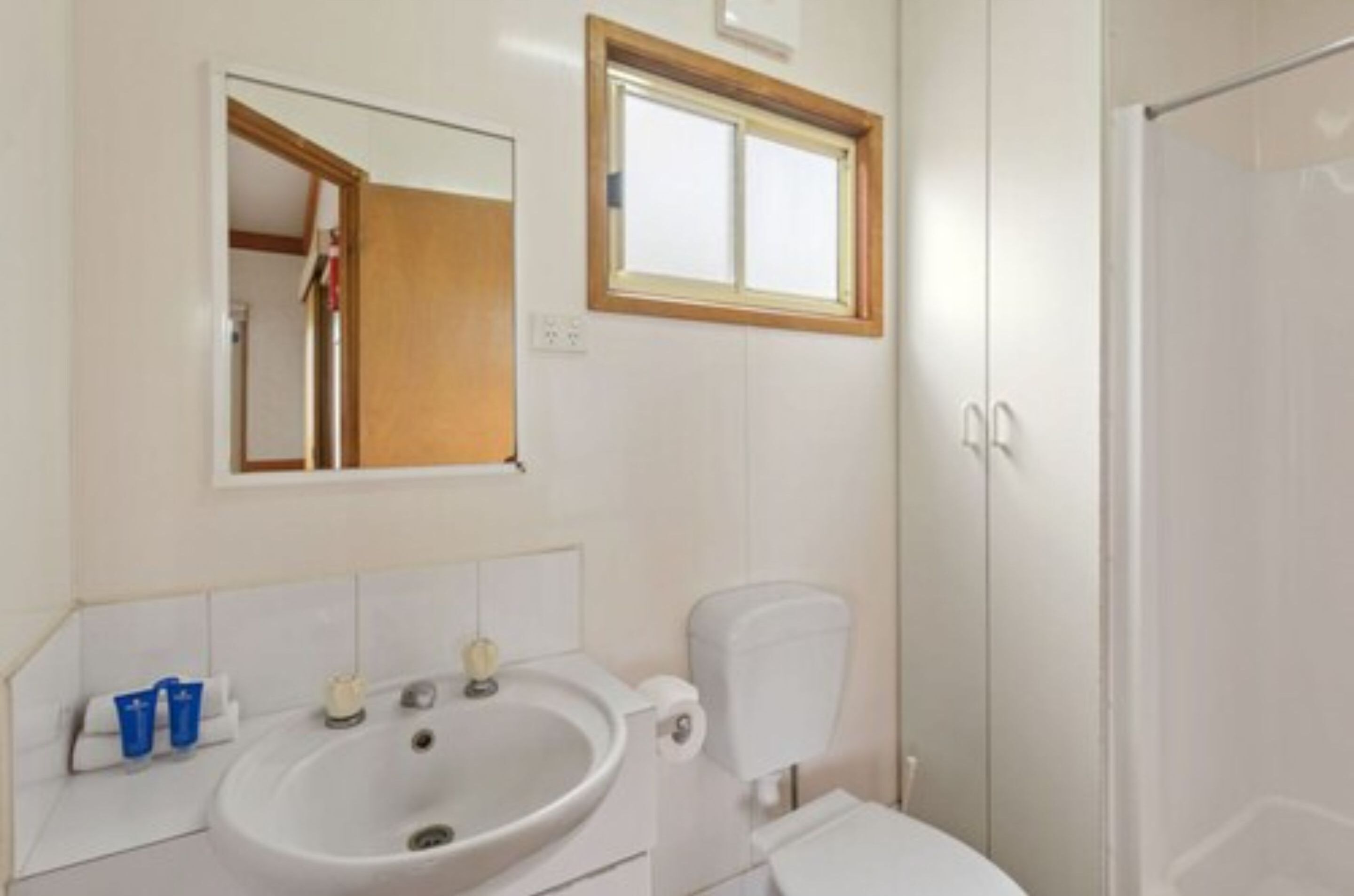 A bathroom with a white sink, a mirror above it, and a toilet. There is a window above the mirror.