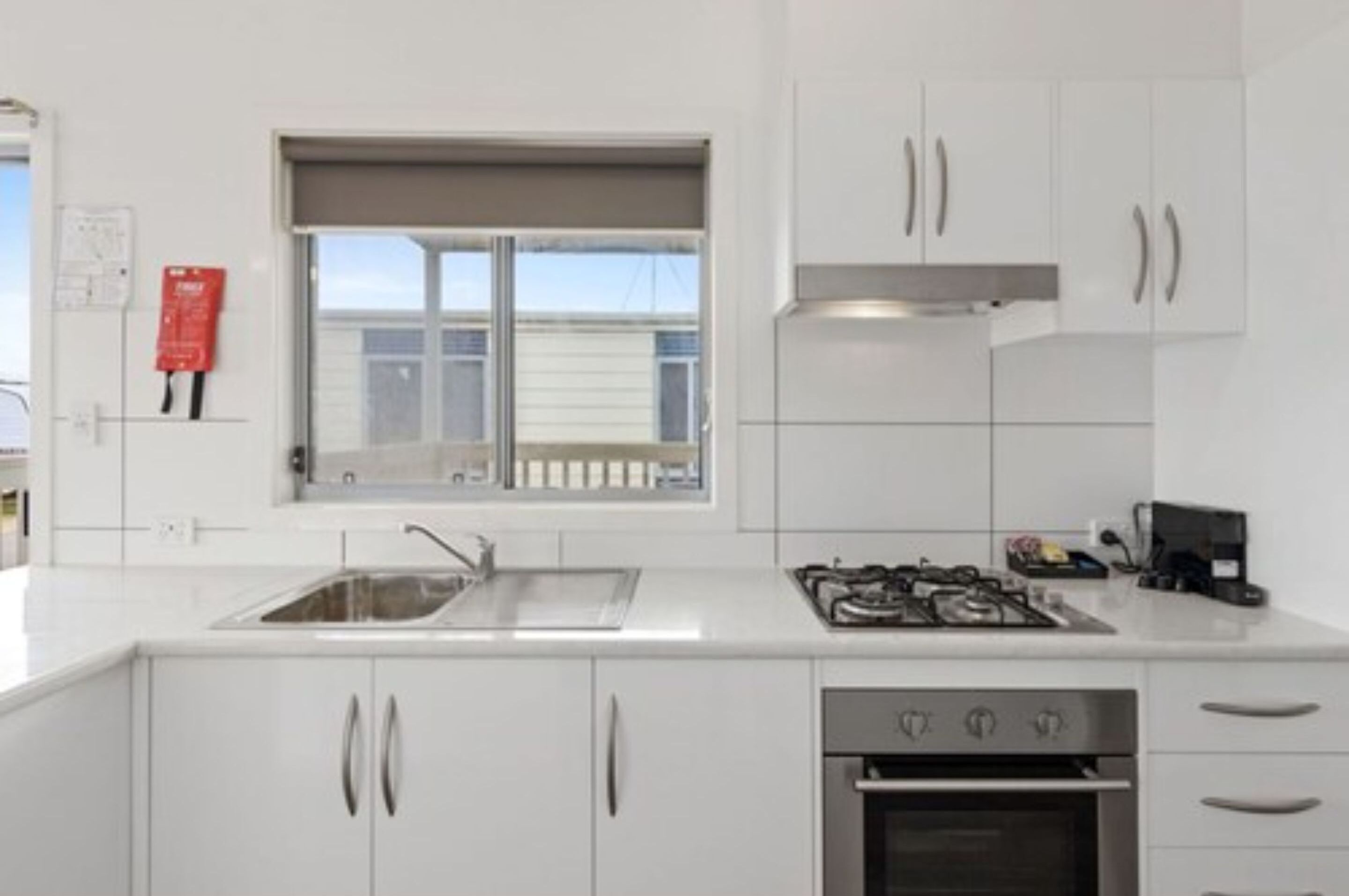 A modern kitchen with white cabinets, a stainless steel sink, a gas stove, and an oven.