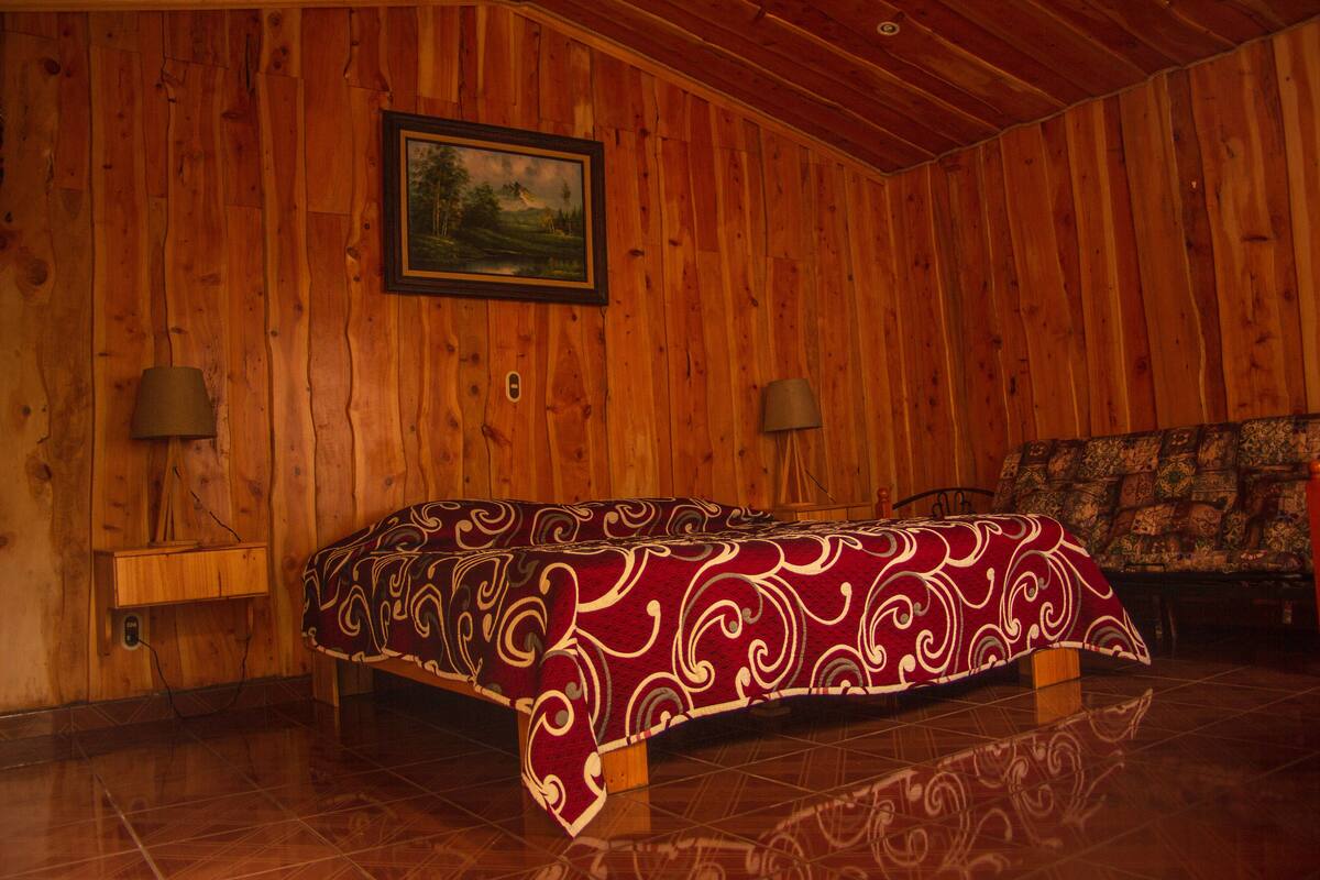 Ein Zimmer mit Holzwänden, einem Bett, zwei Nachttischlampen und einem gerahmten Bild an der Wand.
