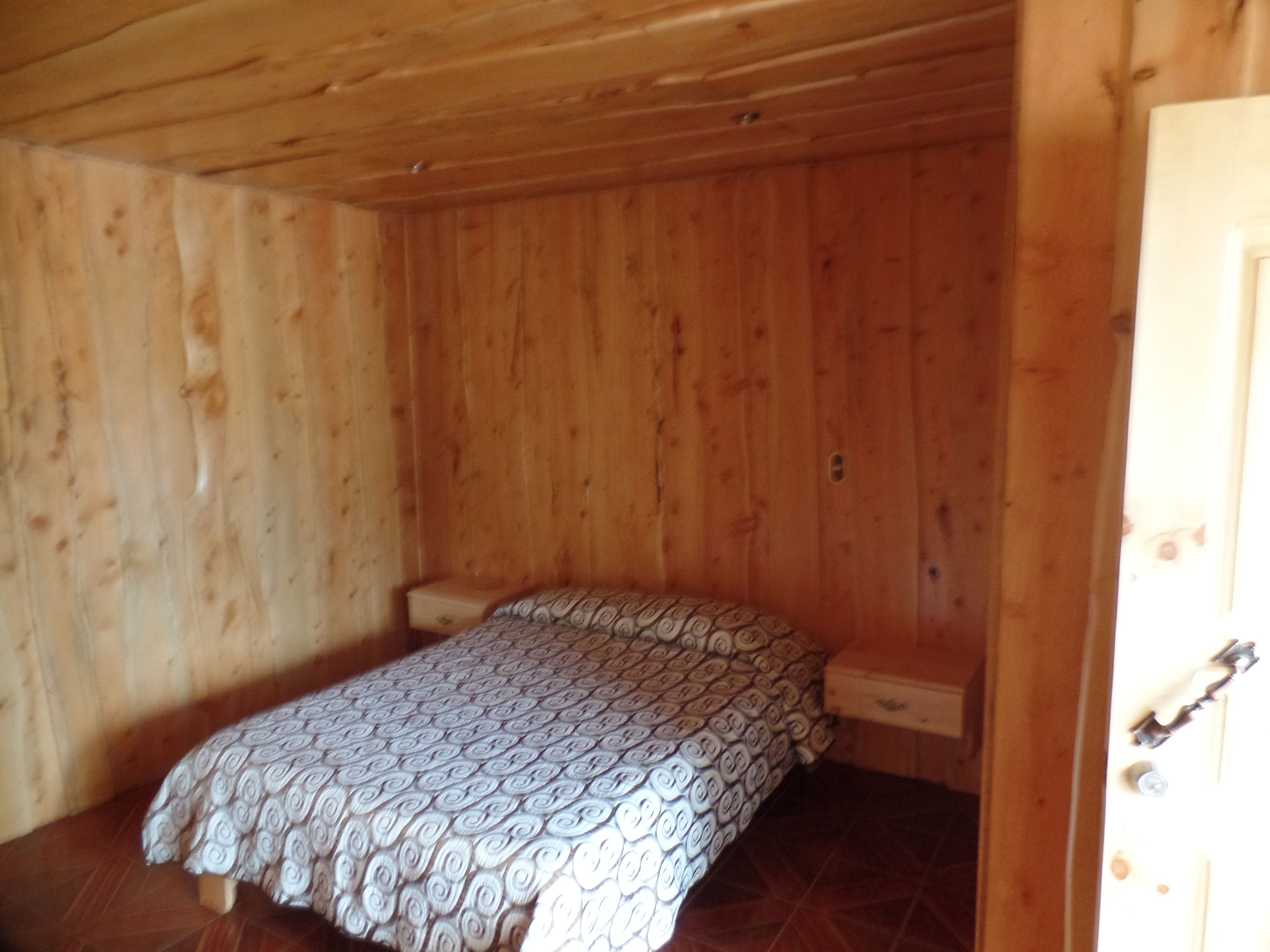 A small, single-bed room with wooden walls and a patterned bedspread.