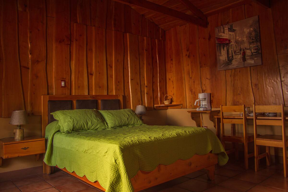 Ein Zimmer einer Holzhütte mit einem Bett, einem Nachttisch, einem Tisch und einem Stuhl.