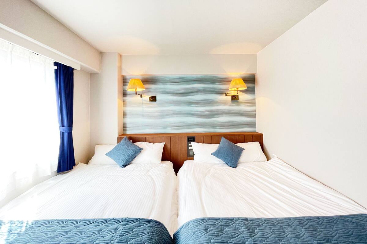 Une chambre d’hôtel avec deux lits, une vue sur la mer et deux lampes fixées au mur.