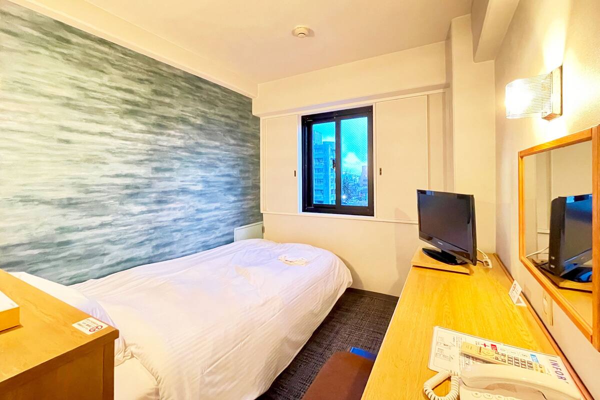 Une chambre d’hôtel avec un lit, un bureau avec un téléphone, une télévision et une fenêtre donnant sur des immeubles.