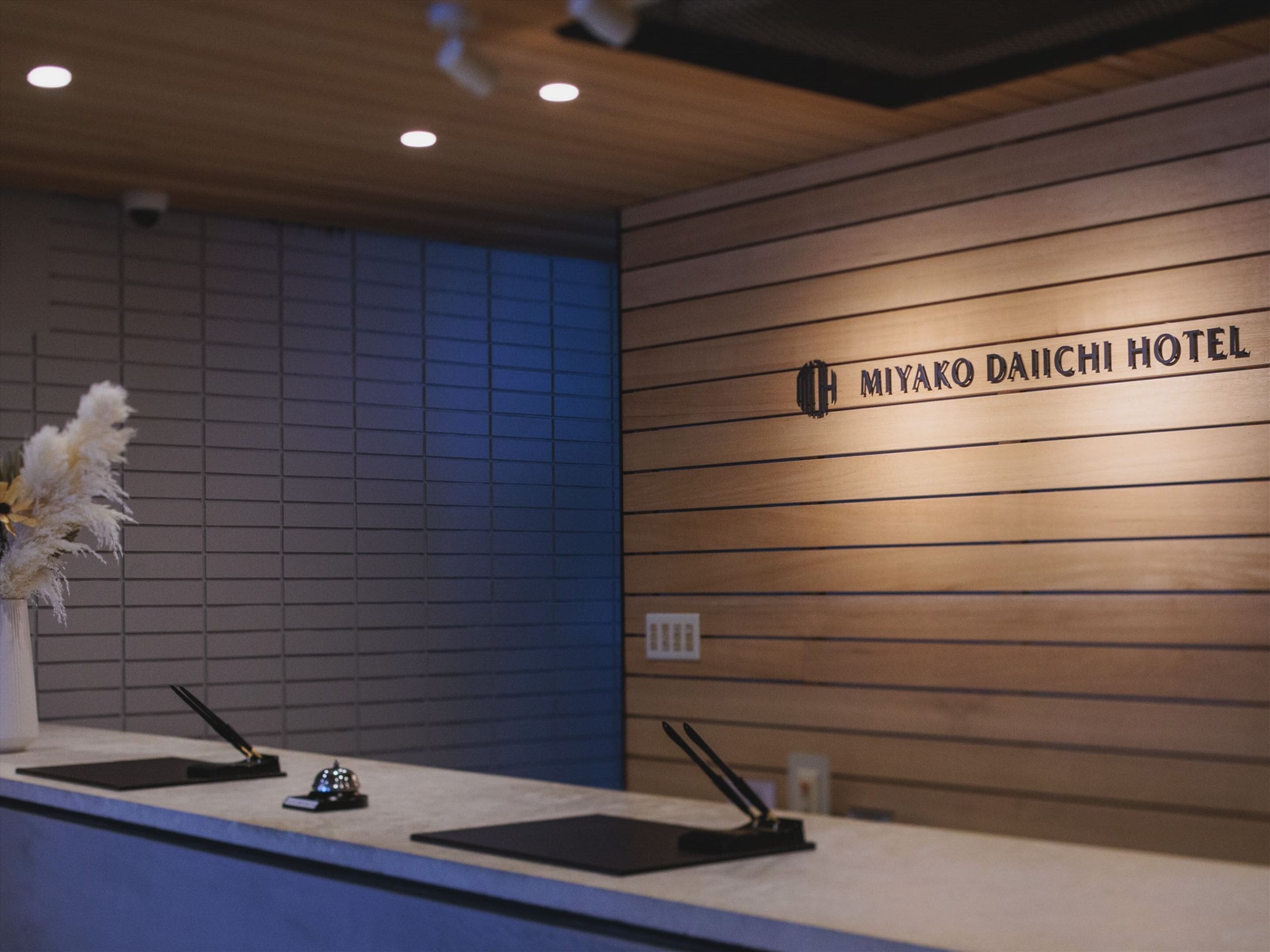 Mostrador de recepción en el Hotel Miyako Daiichi, con un panel de pared de madera y un letrero encima.