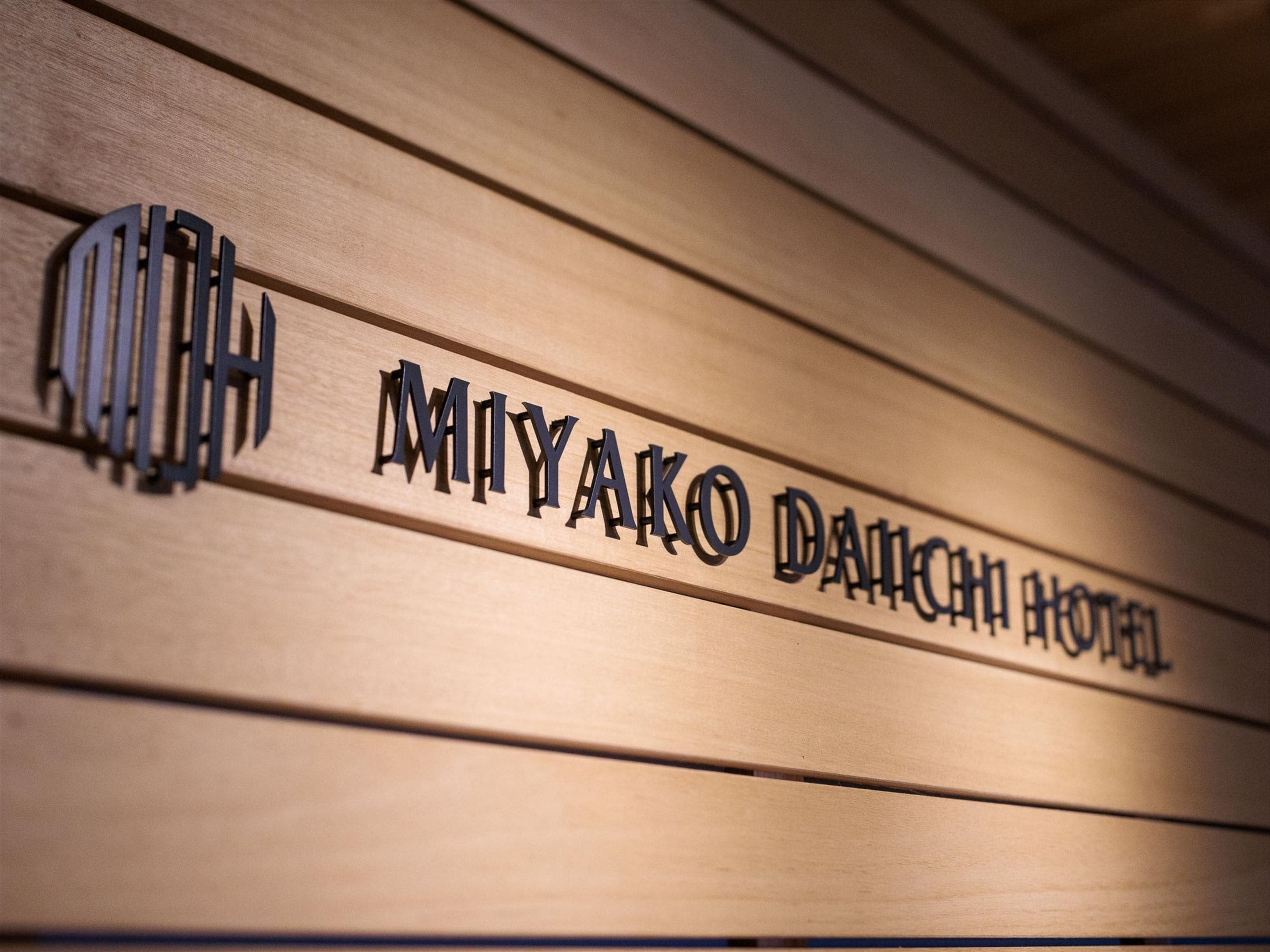 Ein hölzernes Schild mit dem Schriftzug 'MIYAKO DAIKIN HOTEL' in Großbuchstaben.