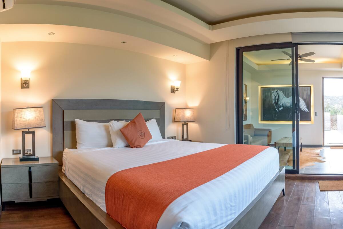 A hotel room with a large bed, two bedside lamps, a nightstand, a glass door leading to a balcony, and a ceiling fan.