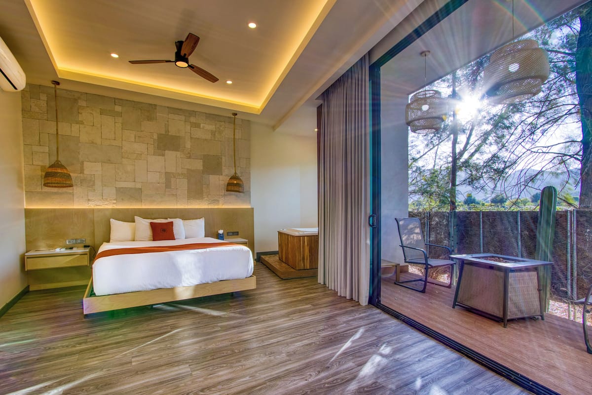 A modern hotel room with a large bed, a ceiling fan, a small table, and a view through a glass door.