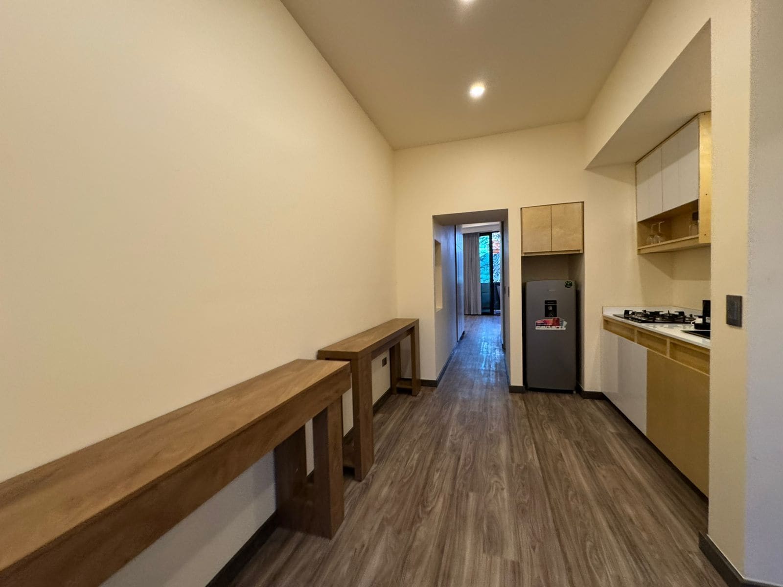 Un pasillo estrecho con un banco de madera, un refrigerador y armarios.