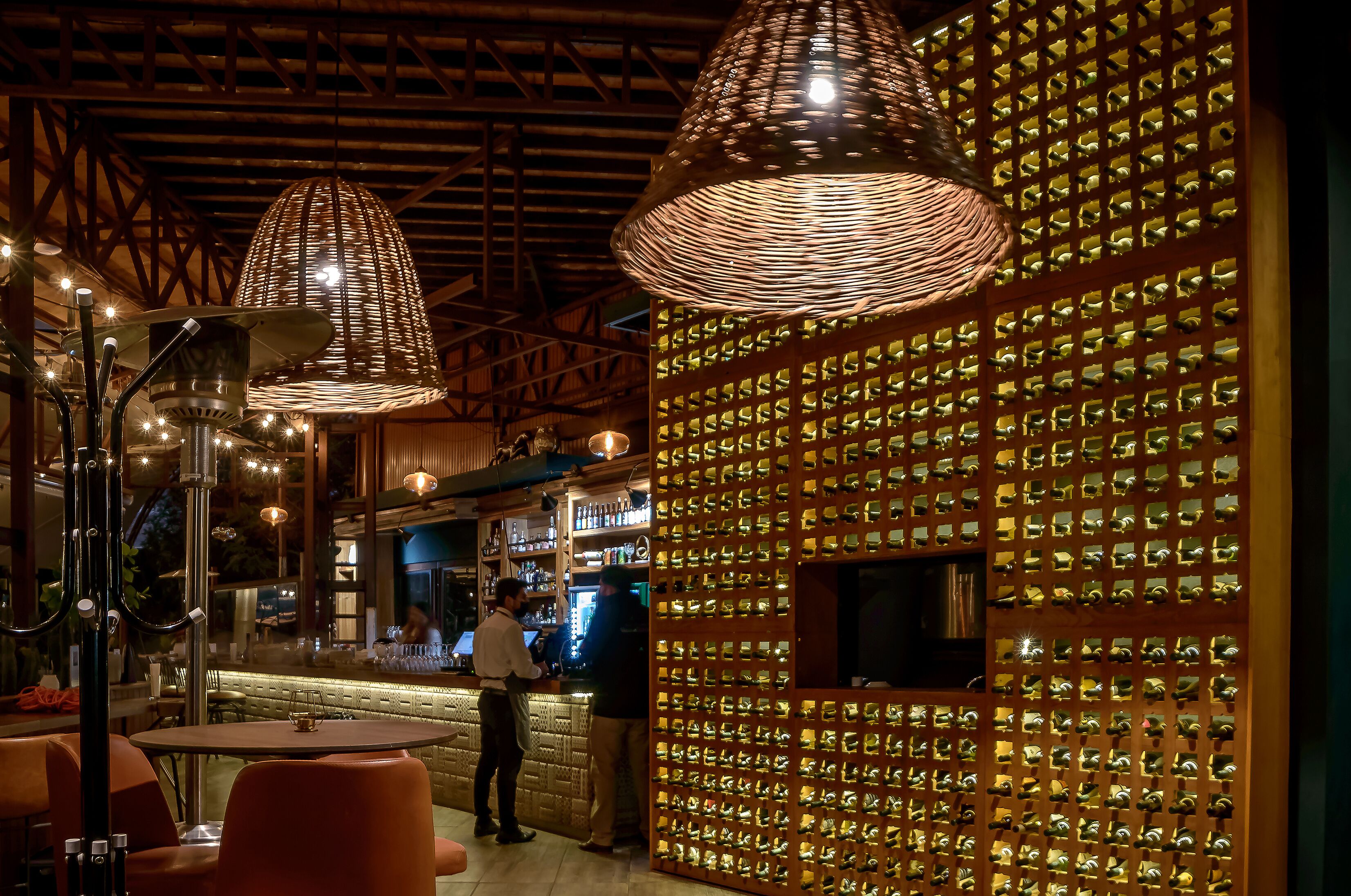 A bar area with a wall of bottles, hanging pendant lights, and a bar counter.