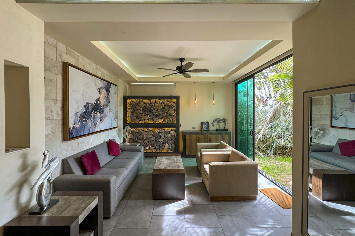 A modern living room with a stone wall, a fireplace, and a large window overlooking greenery.