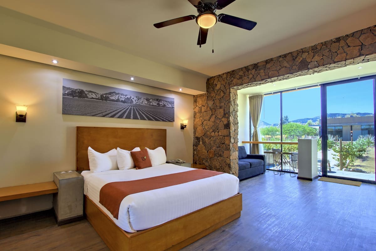 A spacious bedroom with a large bed, a ceiling fan, a stone accent wall, and a view of the outdoors.
