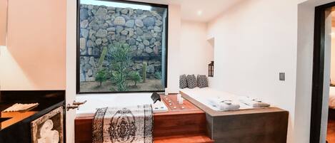 Una habitación moderna con vista a un muro de piedra, un banco de madera y una cama con almohadones estampados.