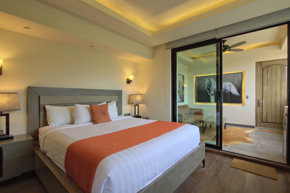 A modern hotel room with a large bed, a glass door leading to a balcony, and a ceiling fan.