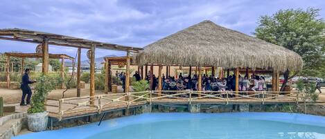 Un área de piscina con una estructura de techo de paja y pérgolas de madera.