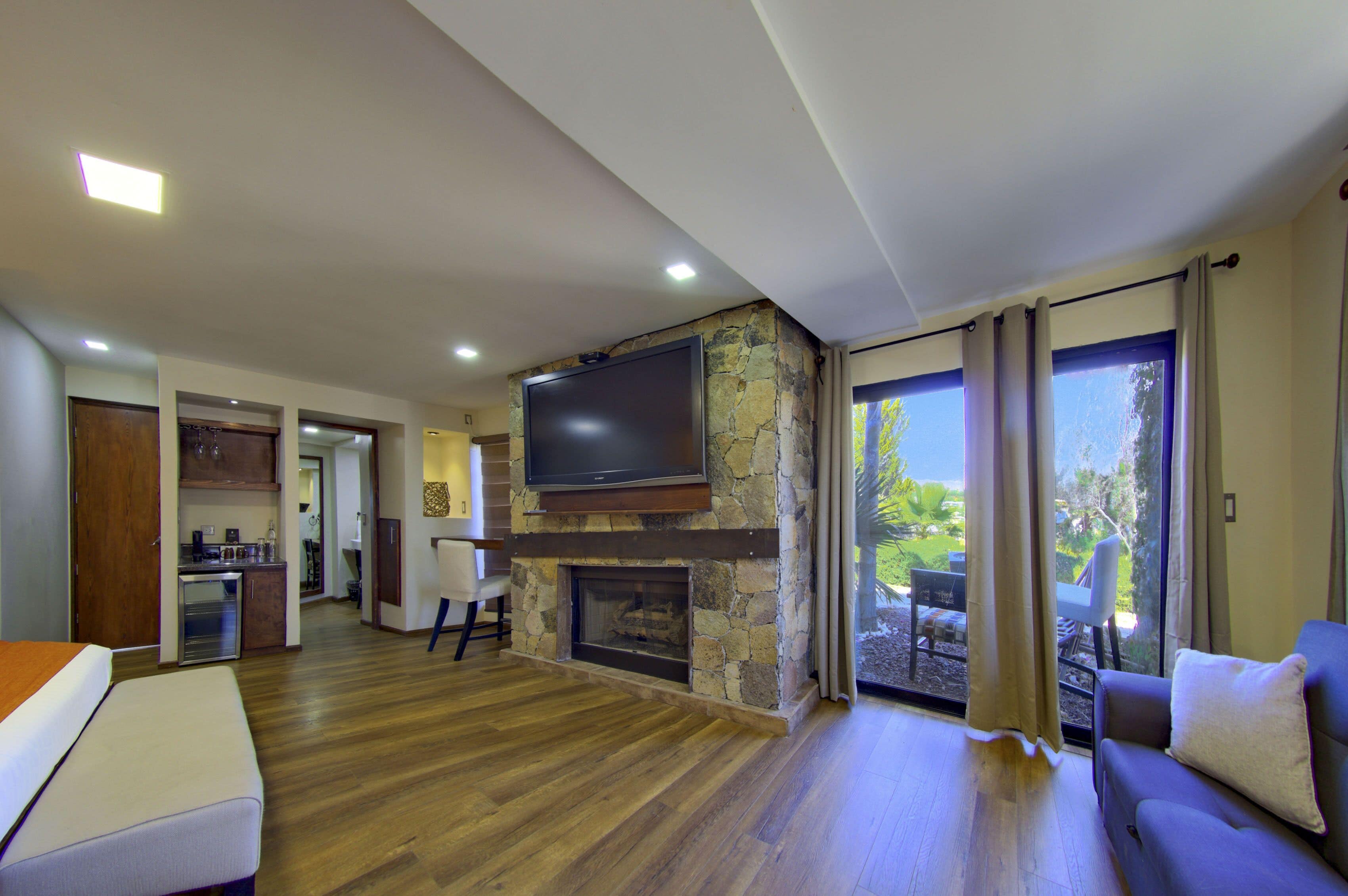 A spacious living area with a stone fireplace, a flat-screen TV mounted above it, and a large sliding glass door leading to an outdoor patio.