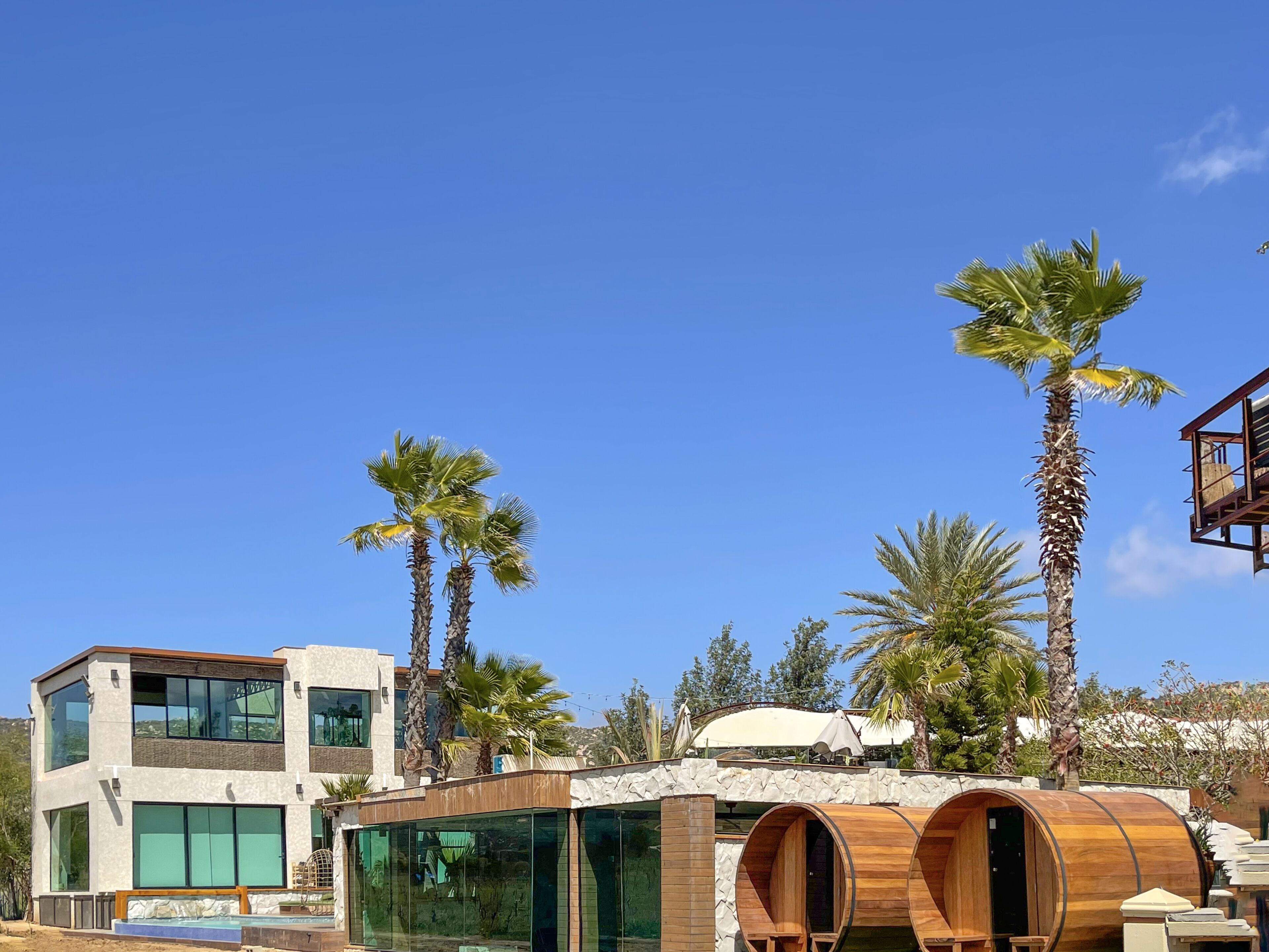 A modern building with large windows, a pool, and wooden barrel-shaped structures.