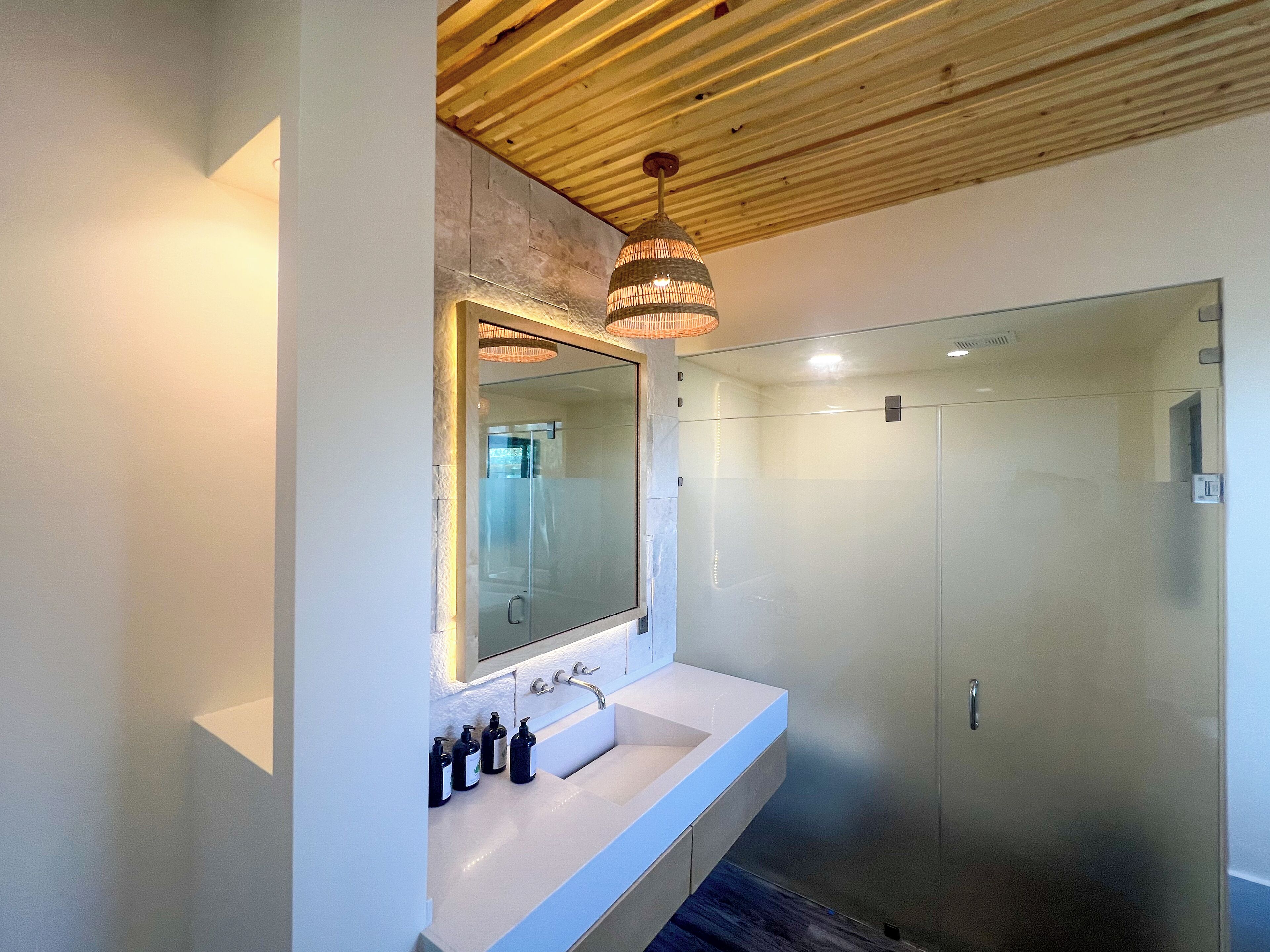 A modern bathroom with a large mirror, white sink, and a glass-enclosed shower.