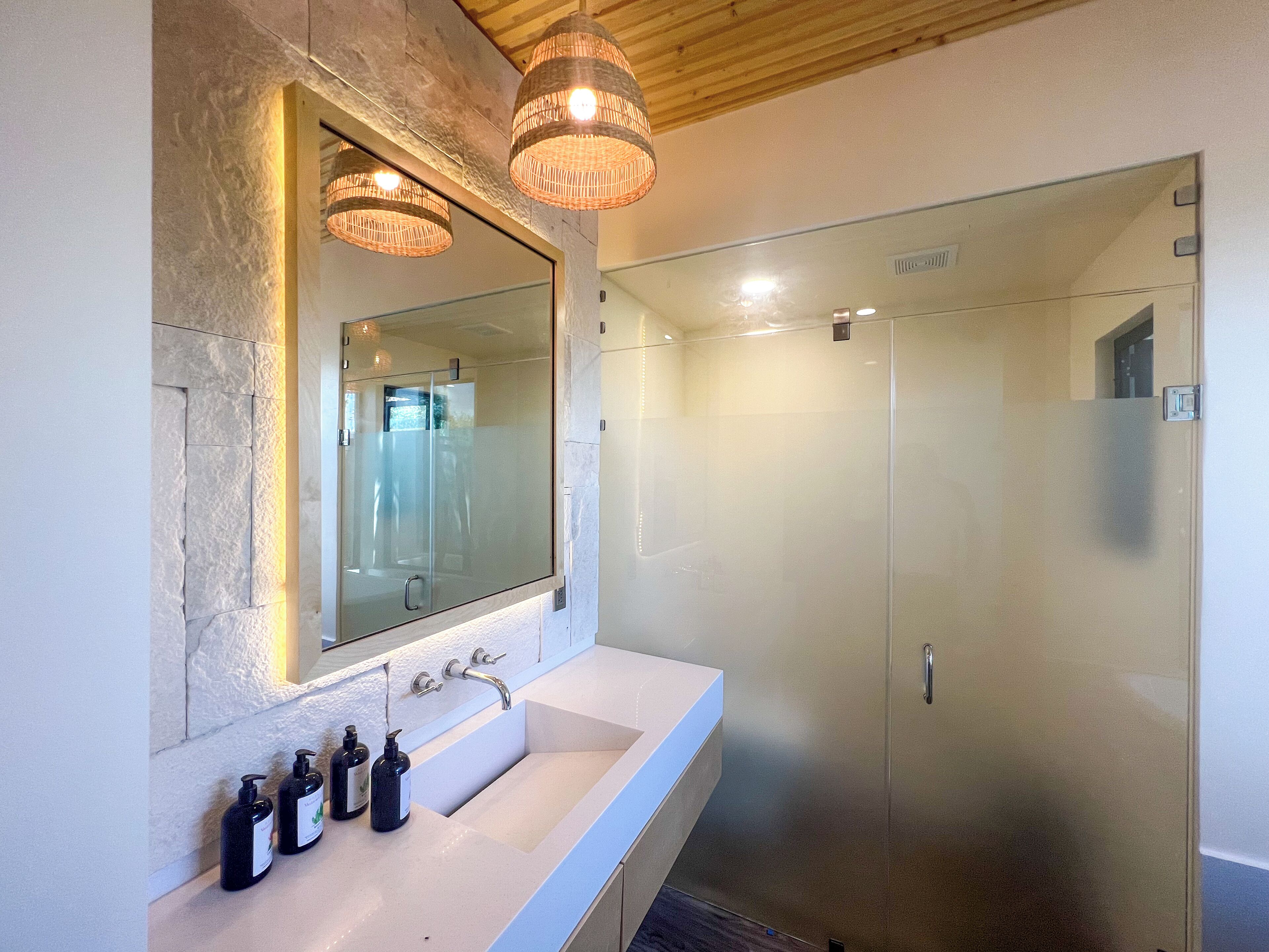 A modern bathroom with a large mirror, a white sink, and two bottles of shampoo.