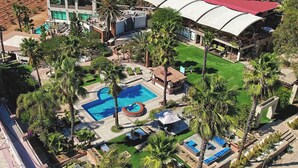 Vista aérea de un complejo turístico con una gran piscina, varias zonas de descanso y un viñedo al fondo.