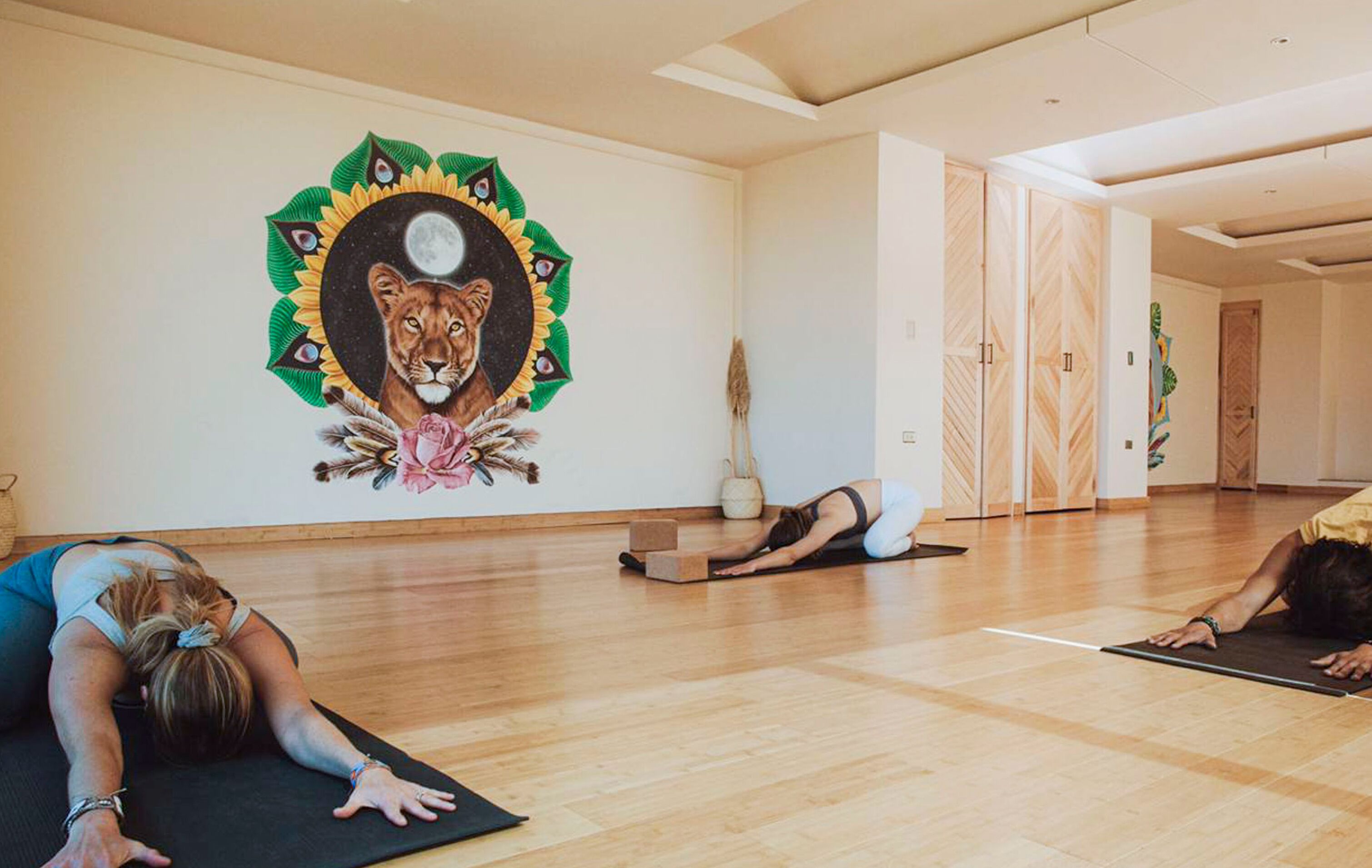 Un estudio de yoga con suelos de madera, un mural de un león y una persona practicando yoga.