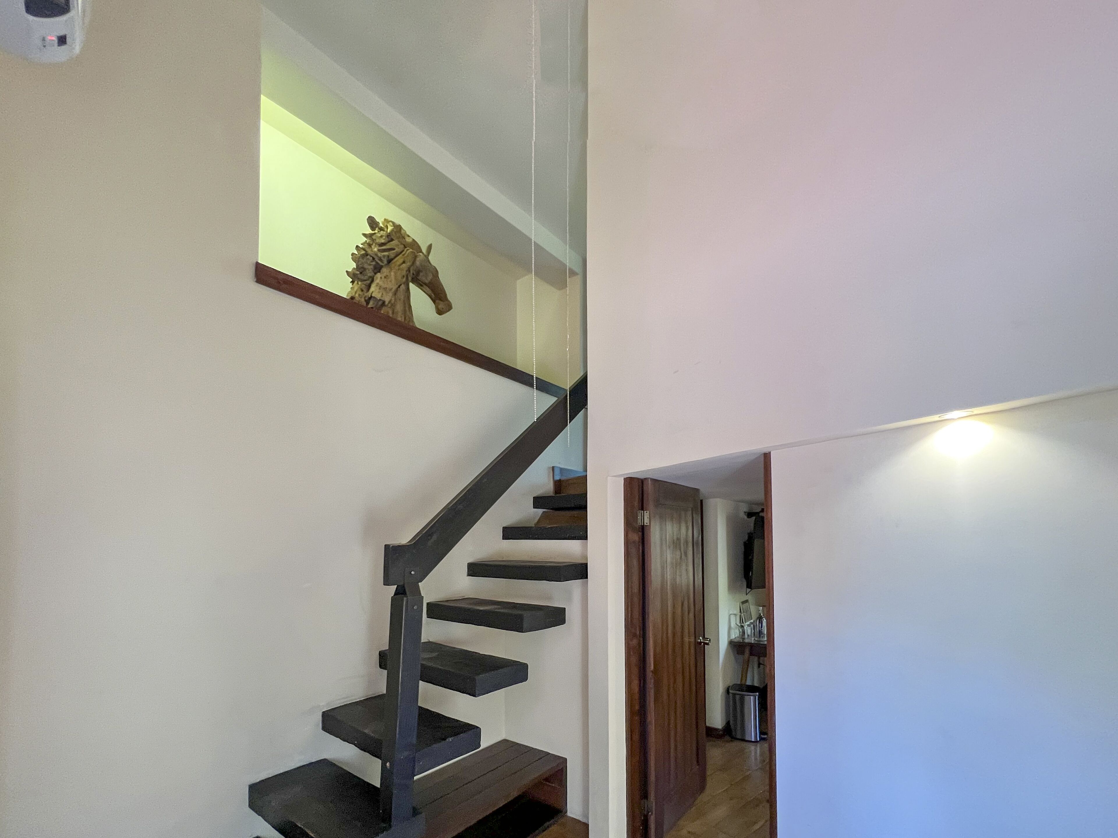 A staircase with a glass railing and a wooden handrail, leading to a landing with a small shelf and a decorative piece.
