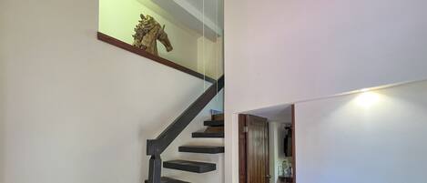 Una escalera con barandilla de vidrio y pasamanos de madera, que conduce a un rellano con un pequeño estante y un adorno.