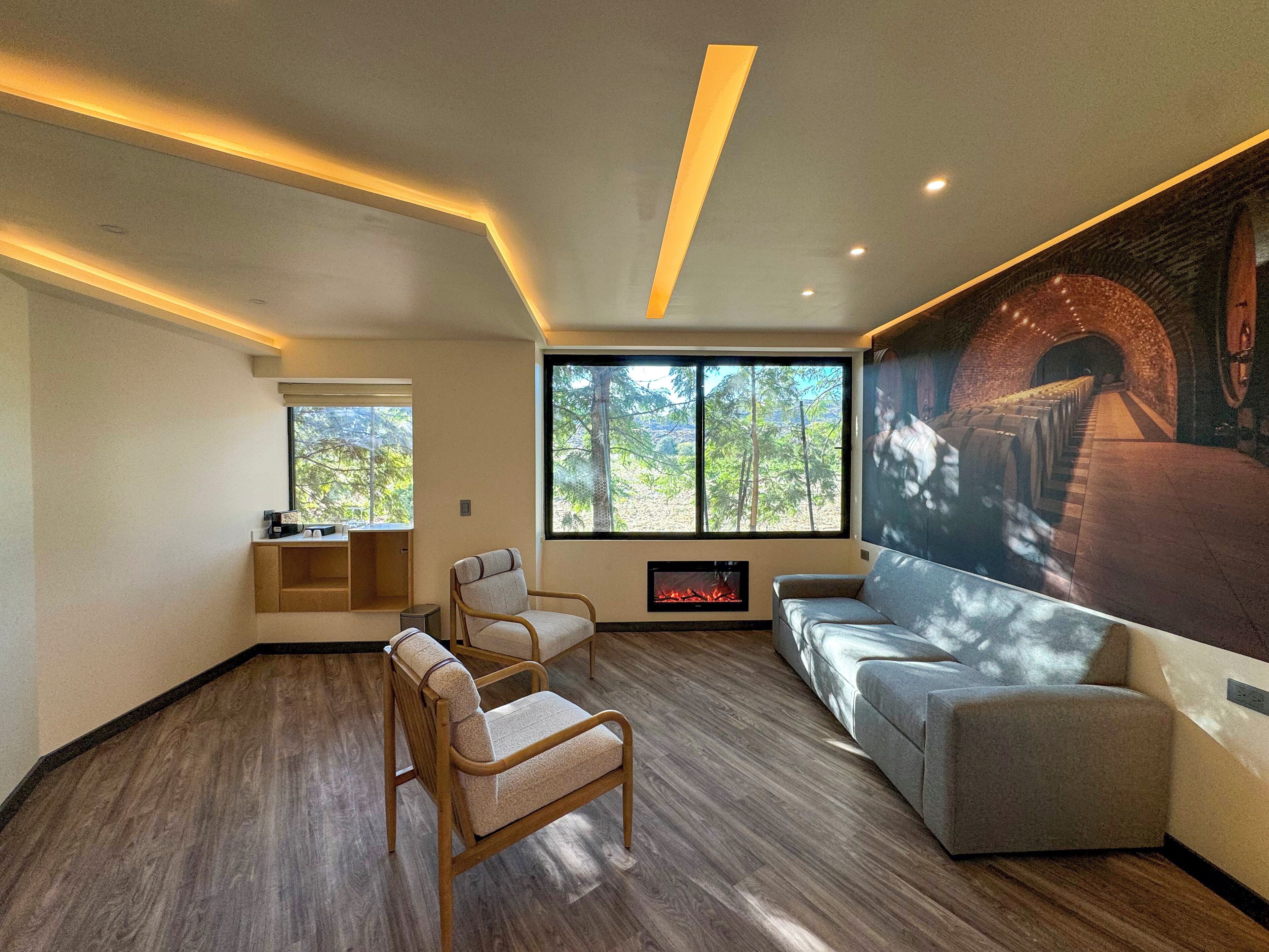 A modern living room with a fireplace, seating area, and a large window offering a view of trees.