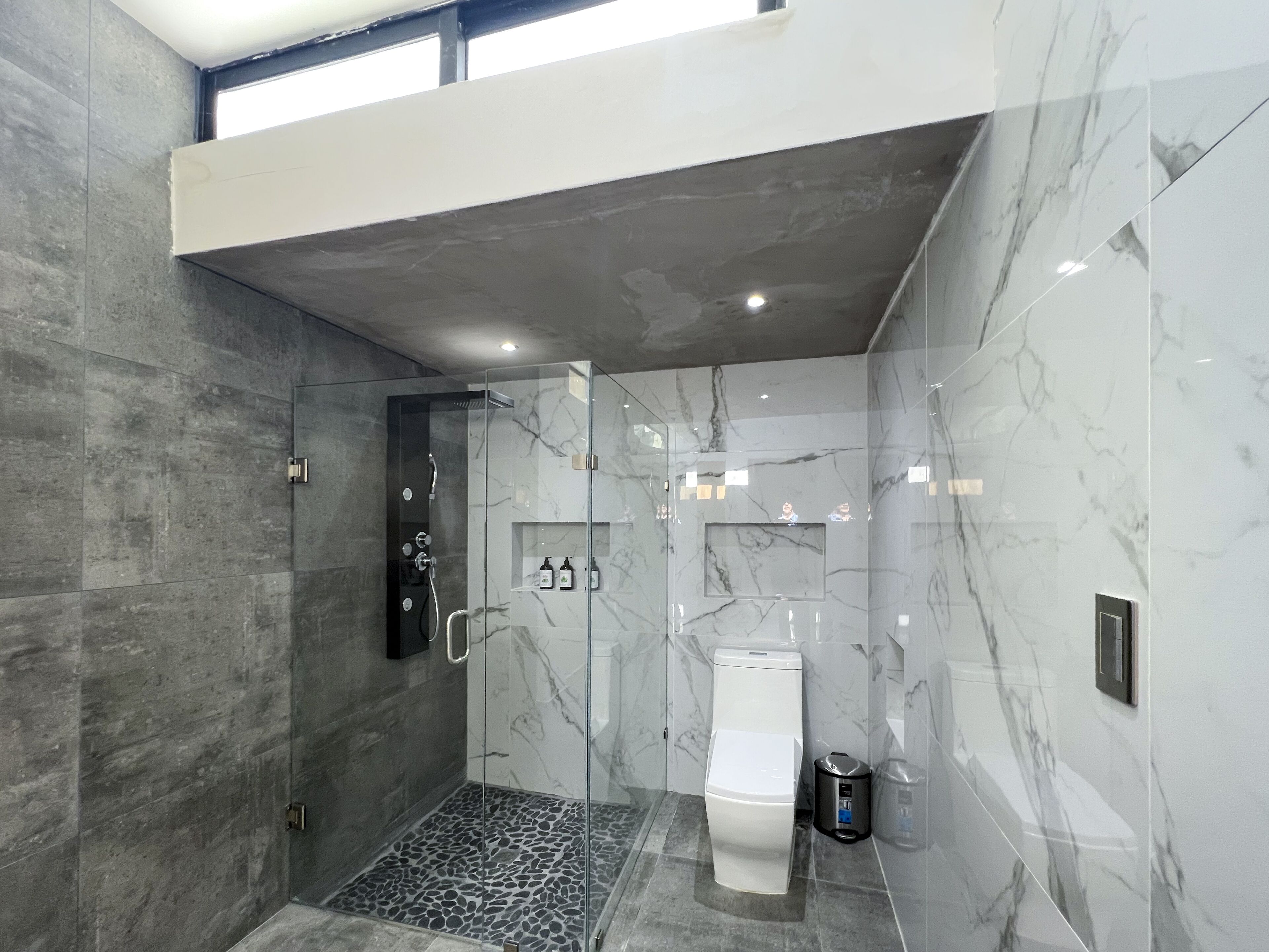 Une salle de bain moderne avec une douche à parois de verre, des toilettes et un mur en marbre.