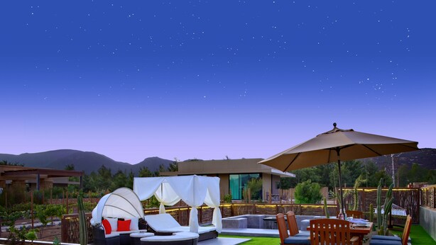 Un patio exterior con una zona de estar, una mesa con un bol de manzanas y vistas al cielo nocturno.
