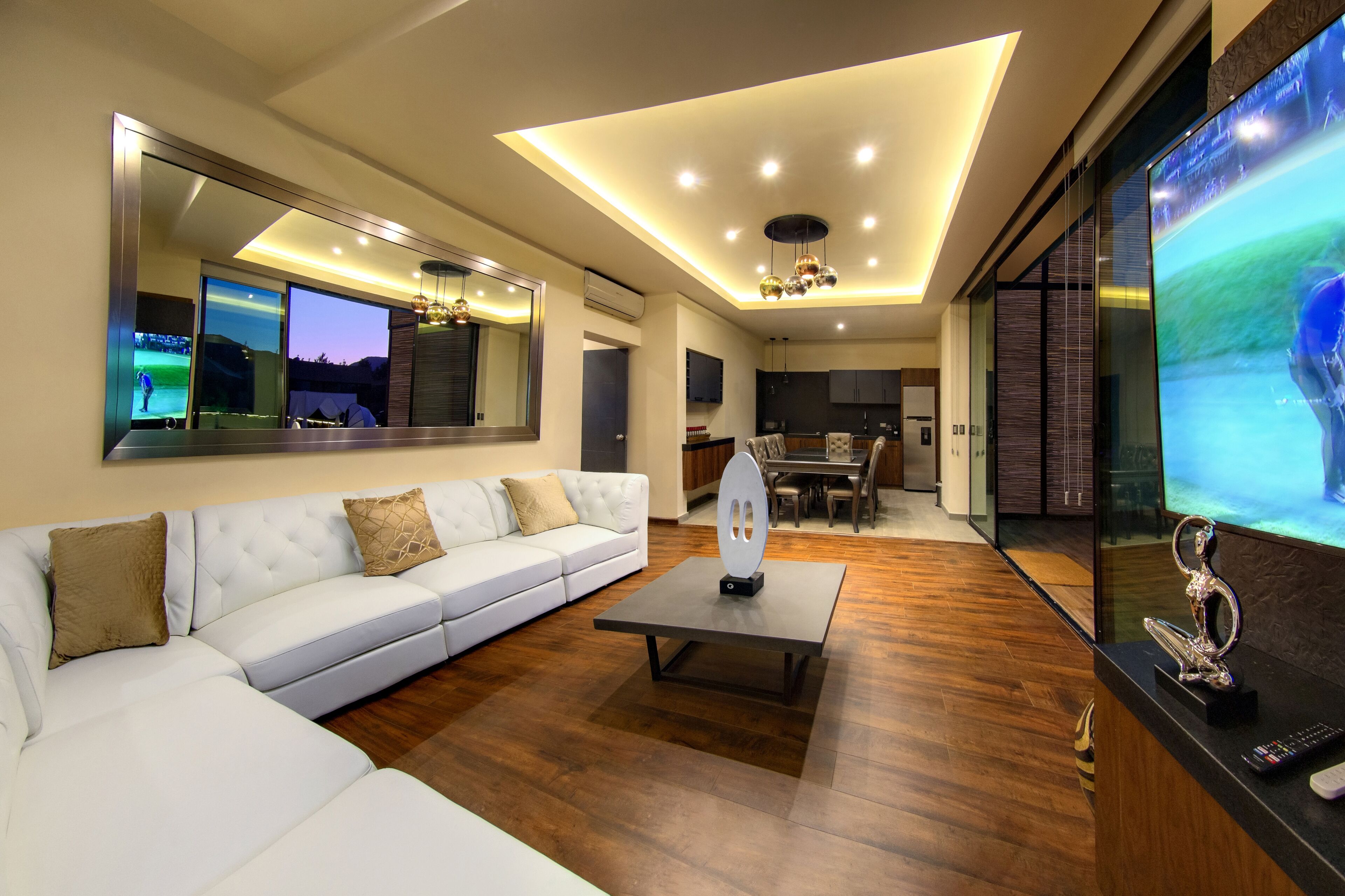 A modern living room with a white sofa, a coffee table, and a large flat-screen TV.