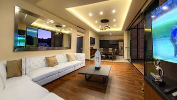 A modern living room with a white sofa, a coffee table, and a large flat-screen TV.