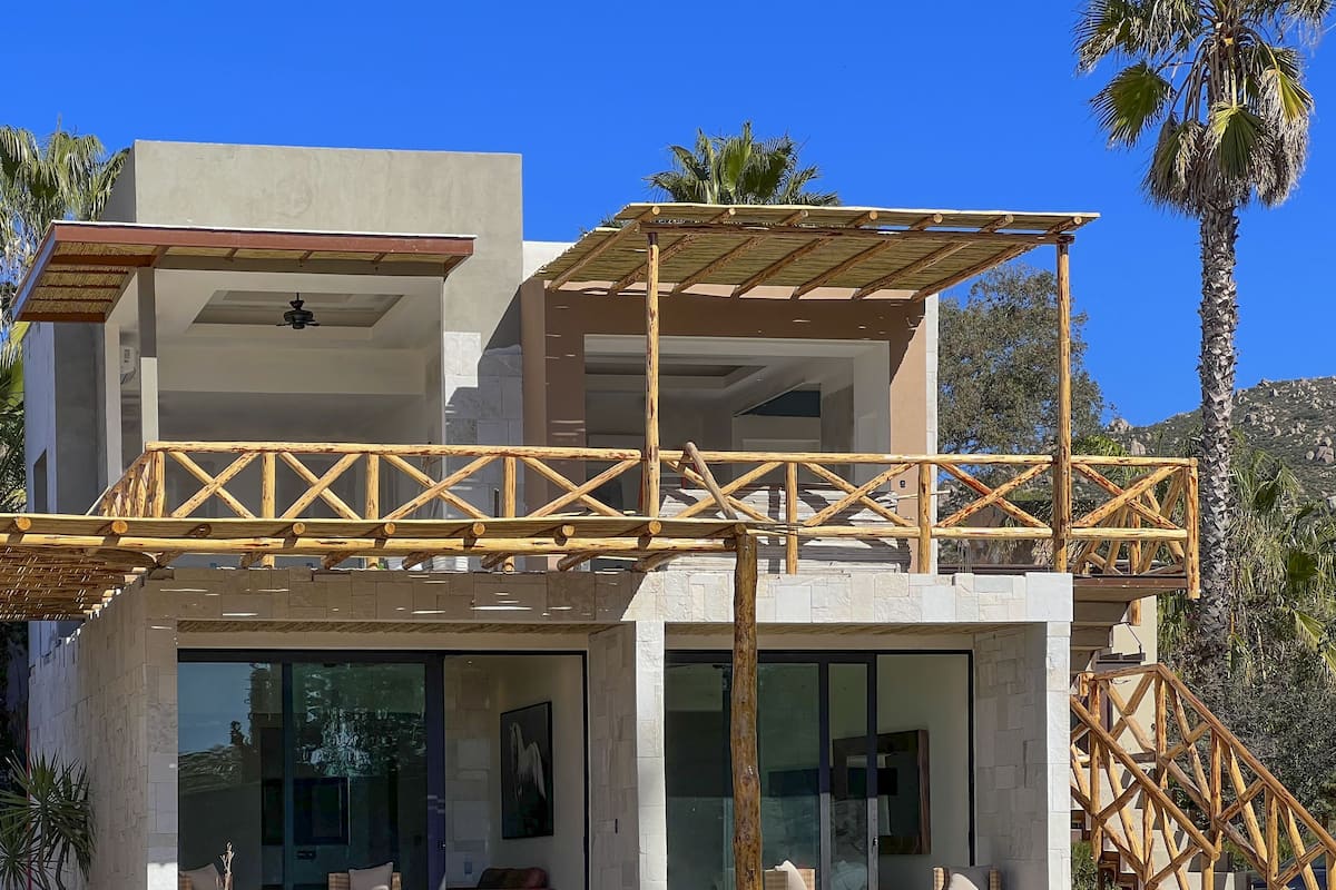A modern two-story building with a wooden balcony structure, large glass windows, and wicker furniture.