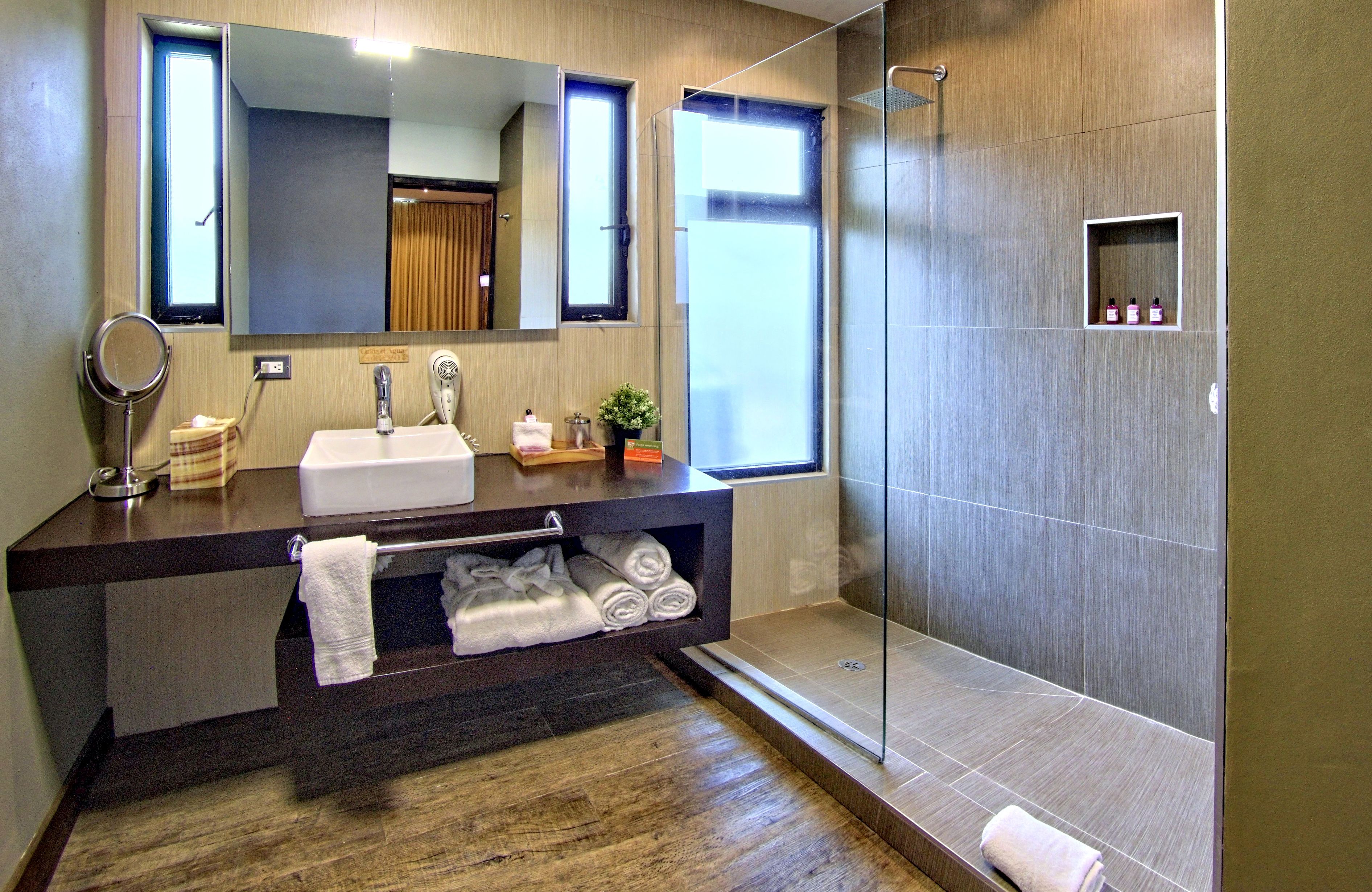 Ein modernes Badezimmer mit einem großen Spiegel, einem Waschbecken, einer Dusche und einer kleinen Ablage mit Pflegeprodukten.