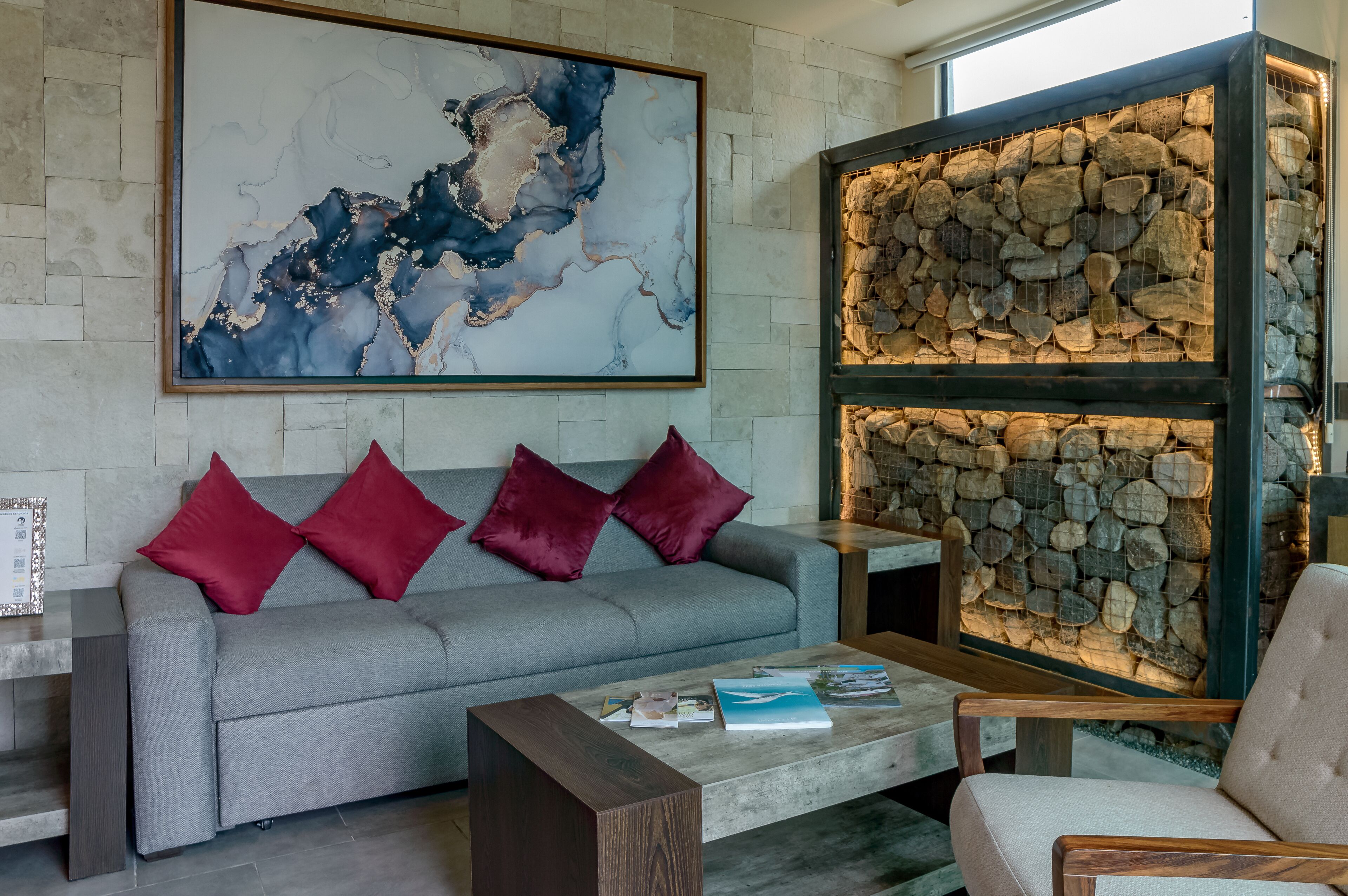 A modern living room with a grey sofa, red cushions, a coffee table, and a large abstract painting.