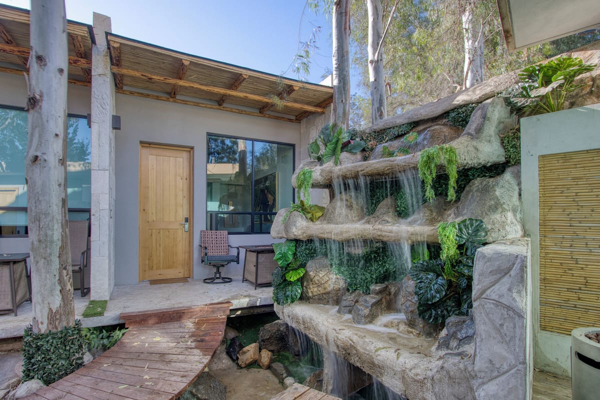 A modern building with a wooden door, a glass wall, and a small waterfall feature.