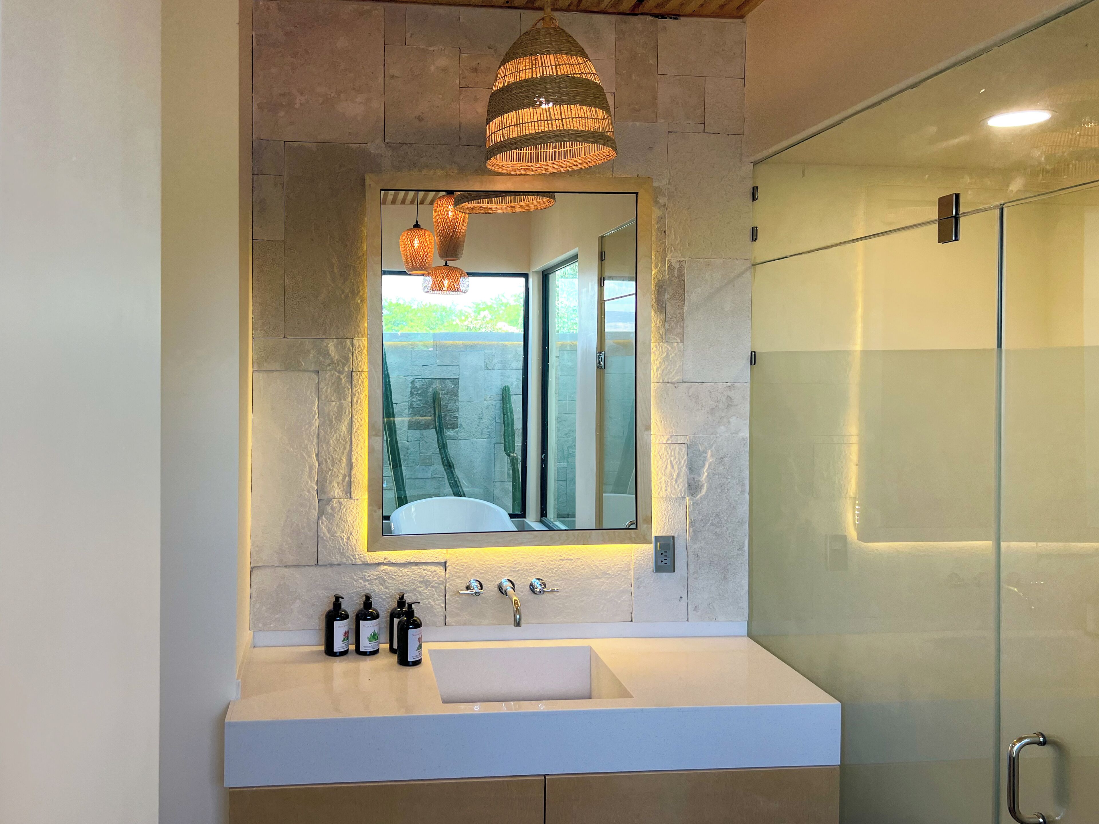 A modern bathroom with a stone wall, a large mirror, a white sink, and a glass shower enclosure.