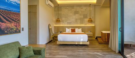 A modern hotel room with a bed, a green sofa, a ceiling fan, and a stone wall.