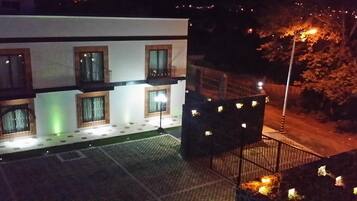 Un edificio de varios pisos con balcones y ventanas, un patio empedrado y una calle con farolas.