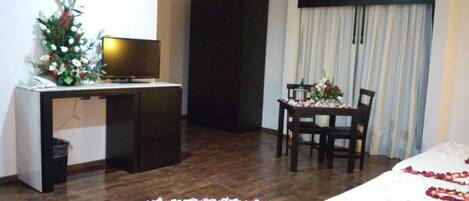 Habitación de hotel con cama, escritorio con computadora, silla y mesa con un florero.