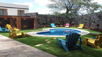 Un jardin avec une piscine, des fauteuils Adirondack, un mur de pierres et une pelouse verdoyante.