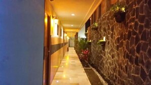 Un pasillo con una pared de piedra a un lado y una pared azul al otro, con suelo de baldosas e iluminación empotrada.
