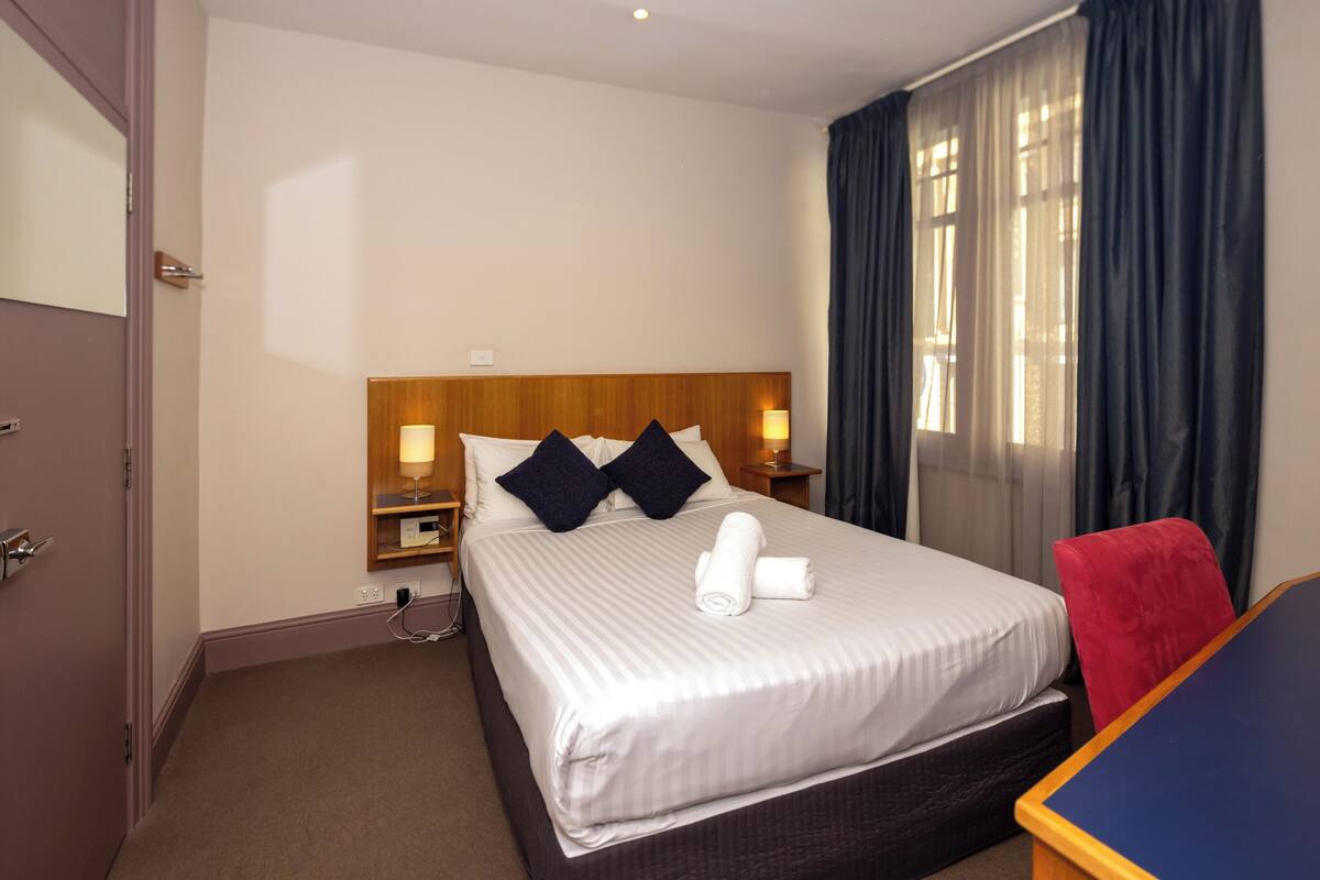 A hotel room with a bed, a nightstand, a desk, and a chair.